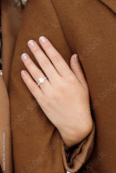 Obraz Wife holds husband's arm while walking in a coat outside. Woman's hand with engagement ring together with mans as a symbol of unity, trust and love. Elegant wedding ring with gemstones on finger