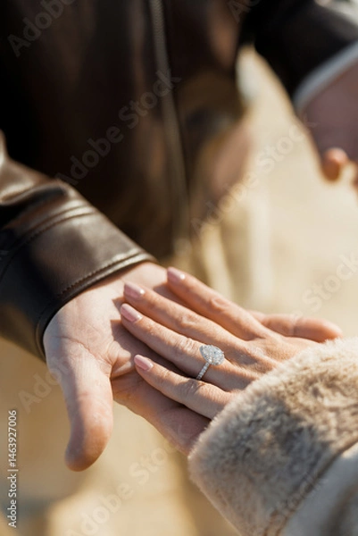 Obraz Couple holding hands together while walking outside. Woman wearing engagement or wedding ring with diamond in the shape of a drop on her finger. Couple's hands in sunlight close-up as a unity