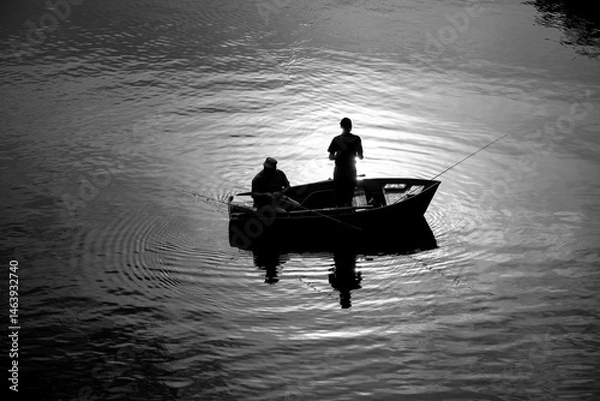 Obraz Two lonely fishermen in a wooden rowing boat fishing in the evening at sunset. Idyllic atmosphere on Lake Hengstey in Hagen. Black and white shot from a bridge.