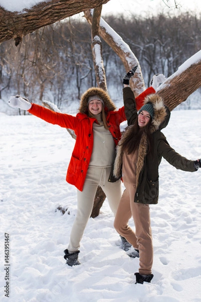 Fototapeta Two girls in winter, in warm clothes, enjoying the snow, outdoor. Cold time of the year, laughter and fun. Winter forest, white glade.
