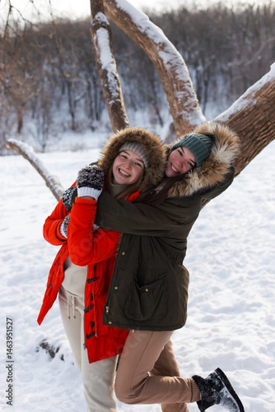 Fototapeta Two girls in winter, in warm clothes, enjoying the snow, outdoor. Cold time of the year, laughter and fun. Winter forest, white glade.