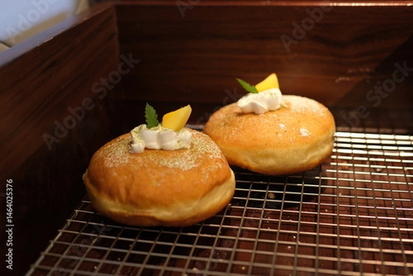 Fototapeta A selection of gourmet donuts topped with a variety of colorful icings, creams, and toppings such as caramel, fruit slices, and sprinkles, arranged neatly on a cooling rack. High quality photo