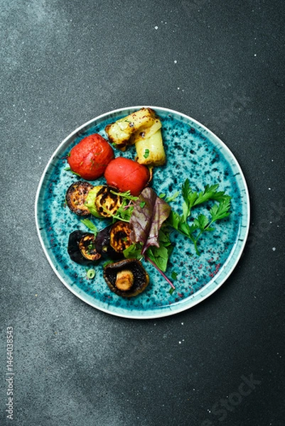 Obraz Grilled vegetables on a blue round plate. On a black stone background.