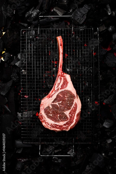 Obraz A raw aged Tomahawk steak is grilled over hot coals. Barbecue. Top view.