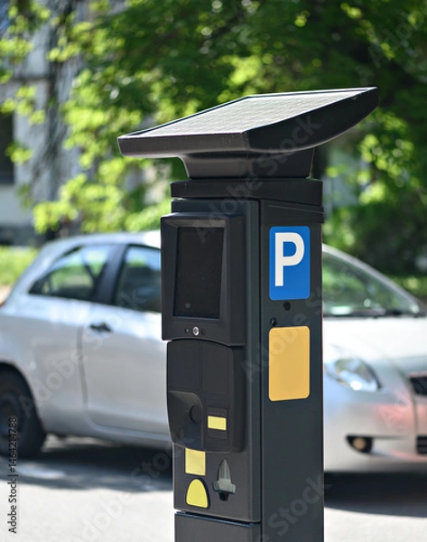 Obraz Solar-powered parking meter stands next to a parked car, showcasing modern urban infrastructure in daylight