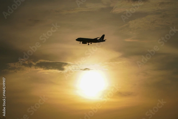 Obraz Silhouette of airplane flying in the sky with sun setting behind