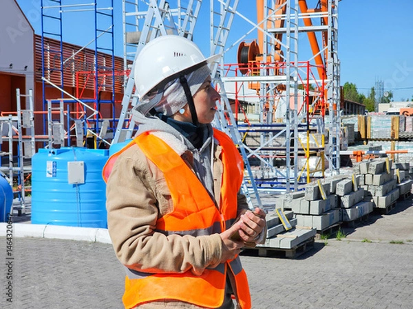 Fototapeta female builder, cranes unloading cargo, engineer designer, woman in orange construction helmet and orange vest, woman working in warehouse, building materials store,