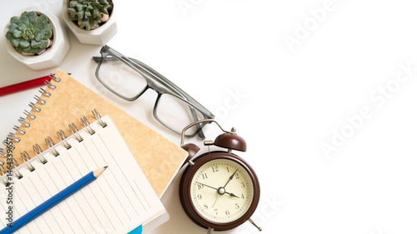 Fototapeta A notebook and pencils sits on a table with an alarm clock and a pair of glasses, isolated on white