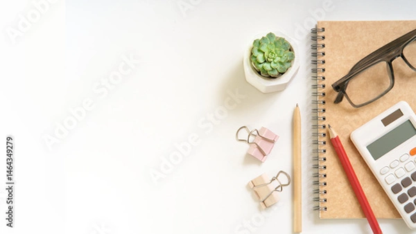 Fototapeta A whitebdesk with a calculator, a pen, a pencil, and a plant. The desk is clean and organized