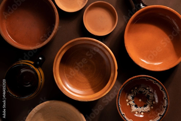 Fototapeta Arrangement of ceramic plates on brown background. Earthenware pottery objects, space for text. 
