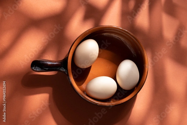 Fototapeta Handmade ceramic plates with home eggs on brown background. Terracotta objects, space for text. Genuine food concept.
