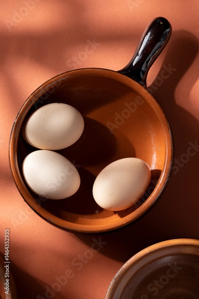 Fototapeta Handmade ceramic plates with home eggs on brown background. Terracotta objects, space for text. Genuine food concept.
