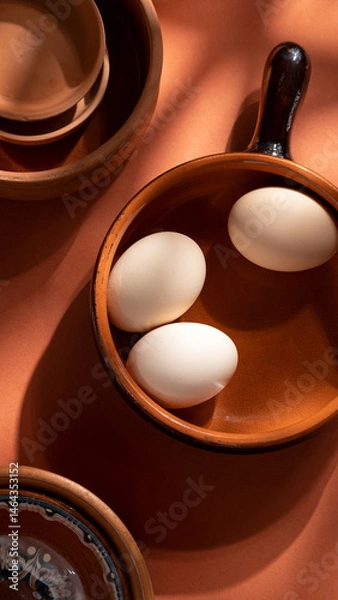 Fototapeta Handmade ceramic plates with home eggs on brown background. Terracotta objects, space for text. Genuine food concept.

