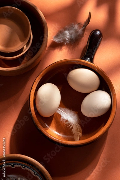 Fototapeta Handmade ceramic plates with home eggs on brown background. Terracotta objects, space for text. Genuine food concept.
