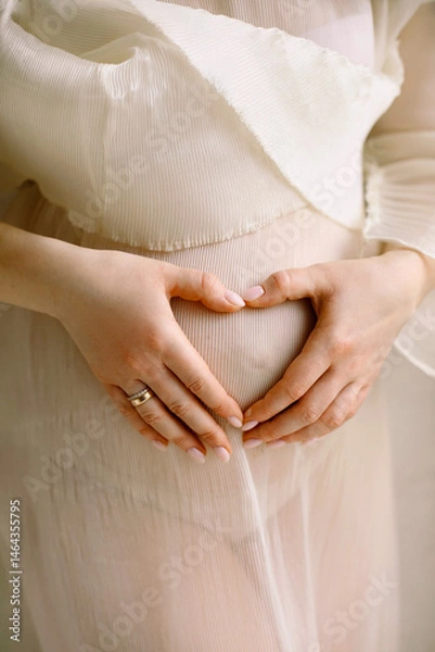 Obraz Close up photo of pregnant woman which makes heart shape with hands on her stomach.  Baby shower. Motherhood concept