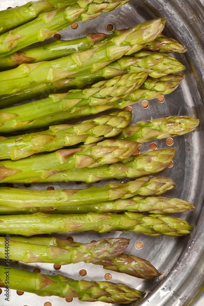 Fototapeta A close-up shows fresh, green asparagus spears arranged inside a metal steamer basket with visible condensation, ready for cooking