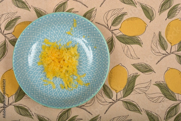 Fototapeta Lemon zest is piled in the center of a light blue patterned plate set on a tablecloth with a lemon design