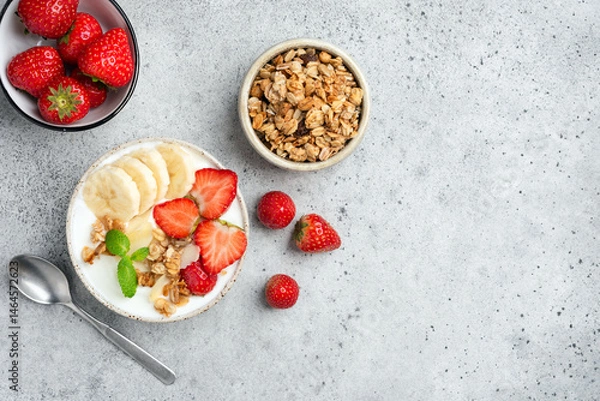 Fototapeta Healthy breakfast bowl with yogurt, granola and fruits on grey table, top view copy space