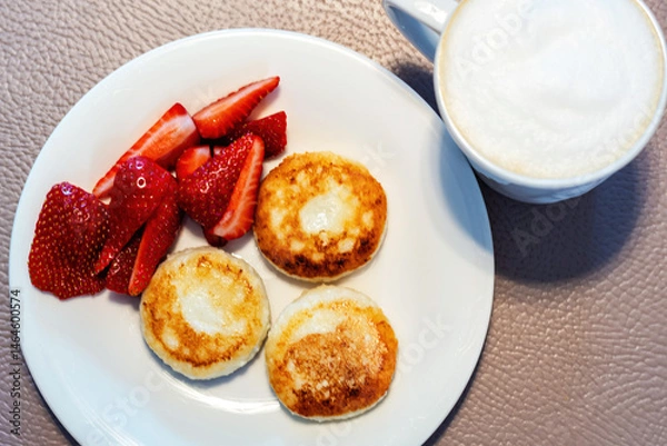 Fototapeta A delicious and healthy breakfast of syrniki served with fresh strawberries and a cup of frothy cappuccino. Traditional Eastern European dish