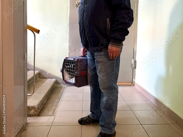 Obraz An elderly retired man holds a cat in a carrier. Pet transportation, traveling with a pet. A close friend of an elderly man