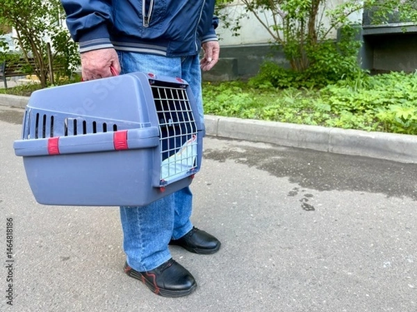 Obraz An elderly retired man holds a cat in a carrier. Pet transportation, traveling with a pet. A close friend of an elderly man