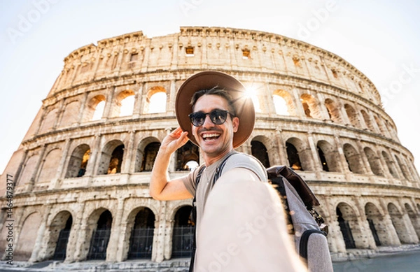 Fototapeta Smiling tourist visiting Coloseum in Rome, Italy - Handsome young man taking selfie with smart mobile phone device - Traveler with backpack enjoying summer vacation - Travel and technology concept