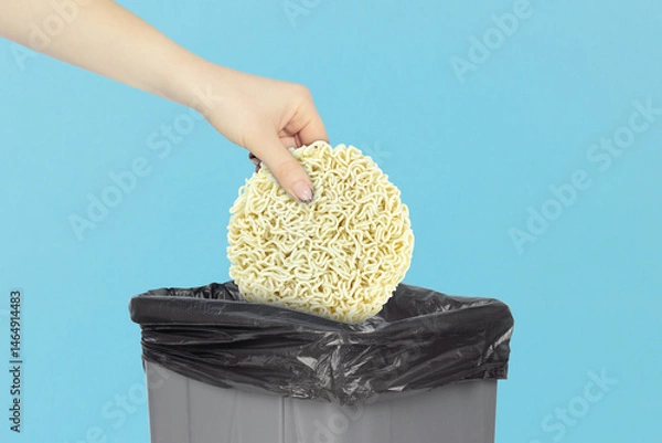 Obraz throw raw instant noodles into the trash can, noodle briquette in hand in front of the trash can, concept of proper nutrition