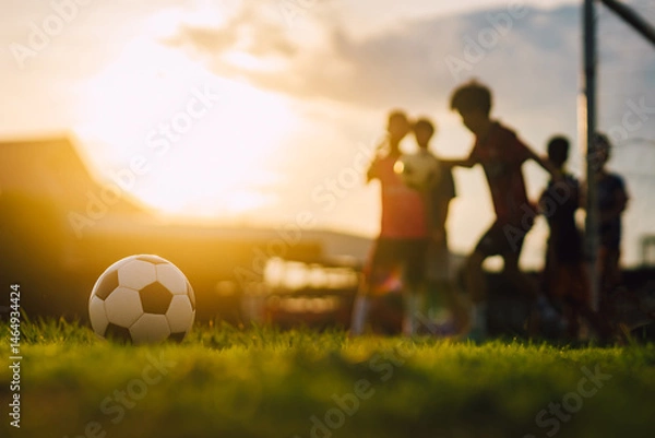 Fototapeta Action sport outdoors of kids having fun playing soccer football for exercise in community rural area under the twilight sunset sky. Picture with copy space.