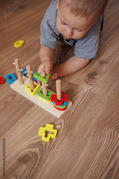 Fototapeta little boy in grey t-shirt playing with educational toy lying on floor. Concept of early child development, learning through play. colorful geometric shapes. close-up of toys