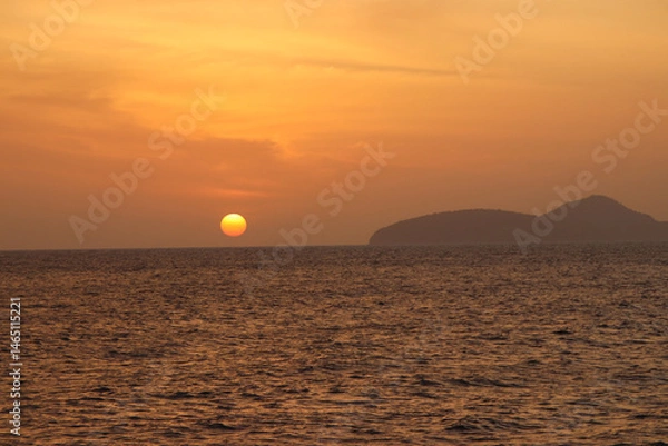 Obraz A breathtaking sunset colors the sky in vibrant shades of orange over the calm waters of the Andaman Sea in Thailand. 
