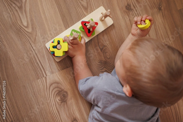 Fototapeta Little boy playing with educational wooden toy at home. top view. Concept of early child development, learning through play and fine motor skills. space for text