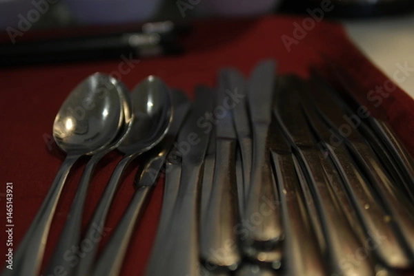 Obraz A rustic flatware set consisting of a spoon, fork, and knife arranged on a grey cloth napkin, evoking vintage charm and functionality. High quality photo