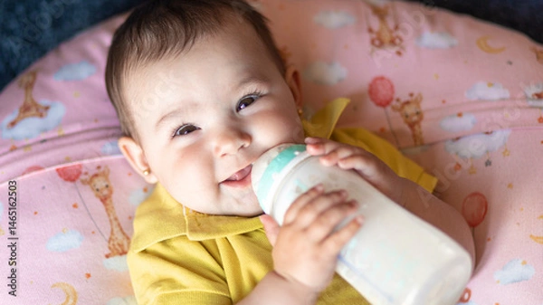 Fototapeta baby drinking from a bottle alone while smiling