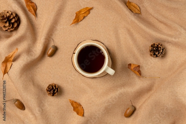 Obraz Mug of tea on brown fabric with leaves as concept background. Flat lay, top view.
