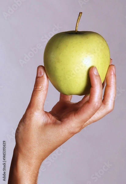 Fototapeta A woman's female hand is holding a green apple isolated on a white background. Symbol of well-being and natural health