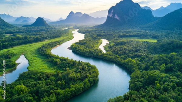 Fototapeta Aerial view of a tropical Southeast Asian river winding through a dense green forest and surrounded by mountain landscapes