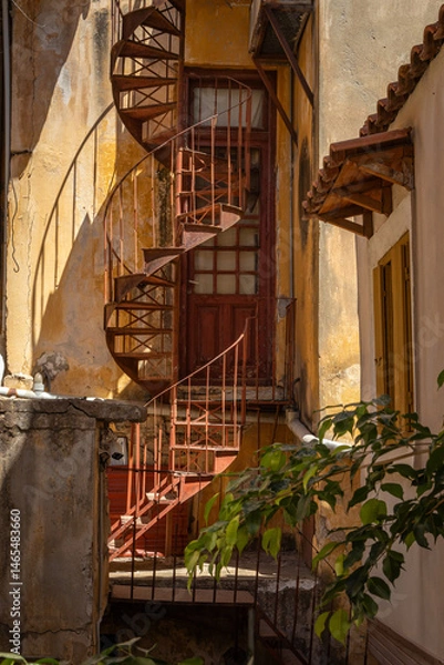 Fototapeta view in alley with steel rusted spiral staircase with shadows in Gythio, Greece