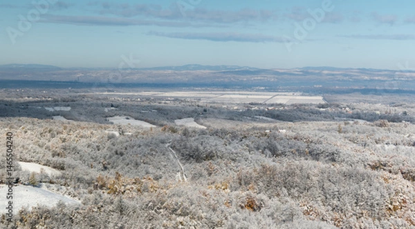 Fototapeta Wintry landscape of countryside, forest covered with frost and snow covered arable land, distant hills in haze
