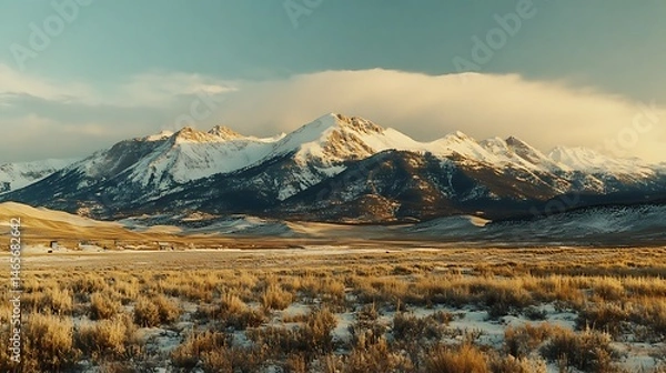 Fototapeta Majestic snowy mountain range over a vast, dry, golden plain.