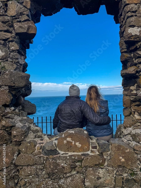 Fototapeta Couple sitting on old ruins, looking out over the ocean