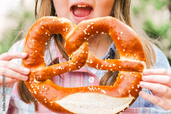 Fototapeta fresh Baked pretzel in the hands of a child. Bavarian traditional pastry. Oktoberfest food traditional.Appetizing pretzel with salt in hands close-up.
