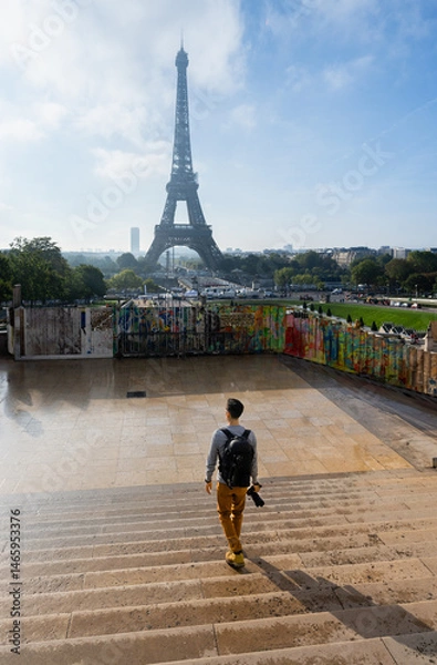 Fototapeta Young Man with Camera and Backpack Walking Toward Eiffel Tower from Trocadero at Sunrise in Paris – Travel Scene