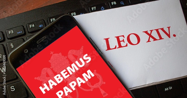 Fototapeta The words habemus papam on a smartphone with the name Leo XIV as the new pope on a piece of paper lying on a keyboard