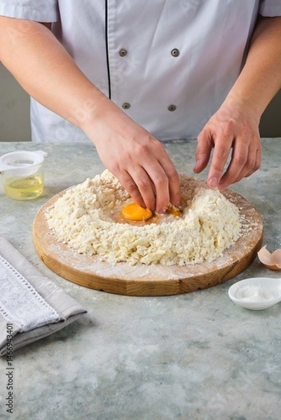 Fototapeta Kneading shortcrust pastry by hand on a wooden board on a grey concrete background. Different types of dough and their preparation techniques.