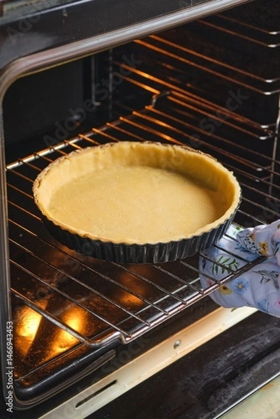 Fototapeta A woman puts rolled out shortbread dough in a black metal round pan into the oven. Making different types of dough. Chef's work.