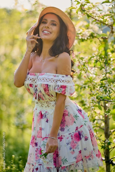 Fototapeta portrait of a beautiful woman in a dress in a blooming apple orchard enjoying a sunny spring day