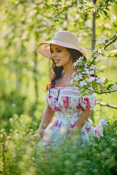 Fototapeta portrait of a beautiful woman in a dress in a blooming apple orchard enjoying a sunny spring day