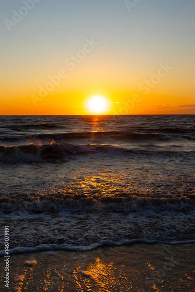 Fototapeta A breathtaking ocean sunset with the sun dipping below the horizon, casting a warm golden glow on the rippling blue water. Serene and picturesque coastal scene.
