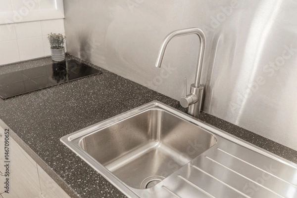 Fototapeta Modern kitchen interior with a stainless steel sink, sleek faucet, and black speckled countertop. Minimalist design with an induction cooktop and light wood cabinetry in a clean, contemporary setting.