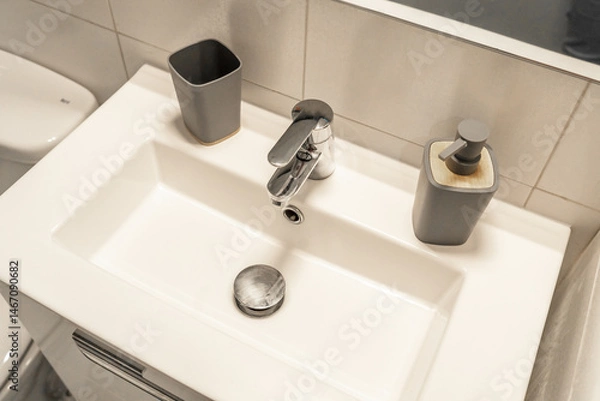 Fototapeta Modern bathroom sink with a minimalist rectangular basin and sleek chrome faucet, complemented by a stylish soap dispenser. 